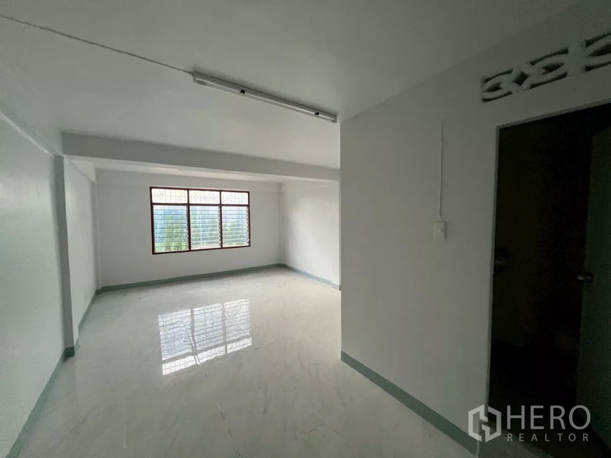 Shophouse for rent in Khlong Toei, Bangkok - Spacious upper room with wide window and glossy tiles overlooking neighborhood greenery.