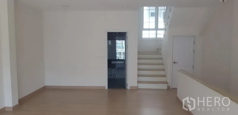 联排别墅 出租在Bang Na, Bangkok - 开放式楼层，浅色木地板，带采光窗的楼梯及室内卫生间门。