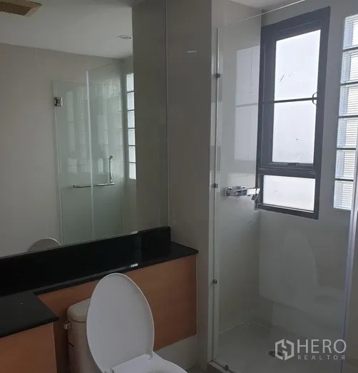 Condominium for rent in Watthana, Bangkok - Compact bathroom with glass shower, window and large vanity mirror.