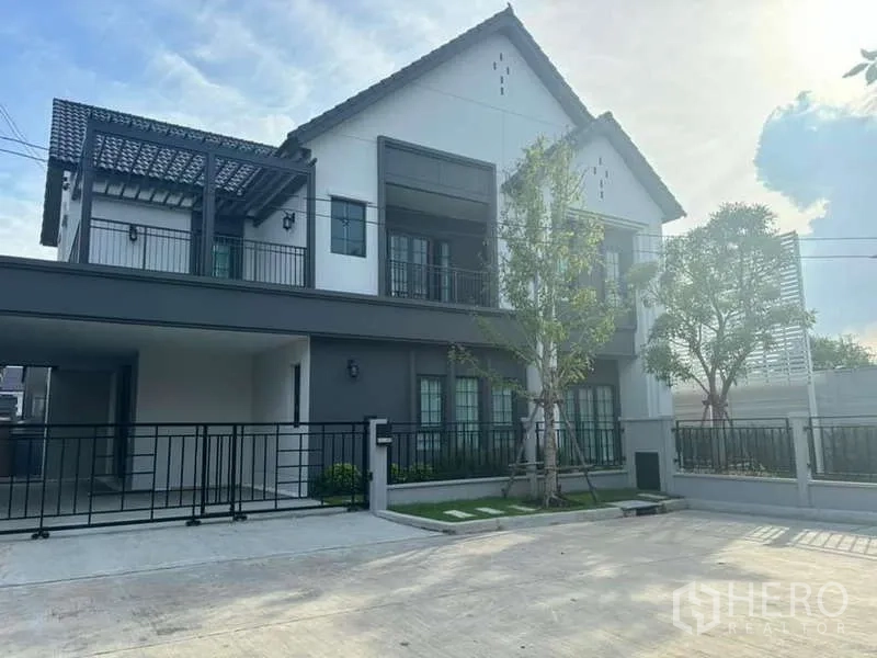 Detached House for rent in Bang Phli, Samut Prakan - Two-storey modern detached house with gated driveway, balcony and pergola under a bright sky.