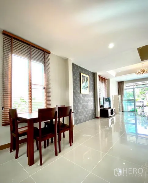 Townhouse for rent in Prawet, Bangkok - Dining area with wooden table by tall windows and view toward the living space and terrace.