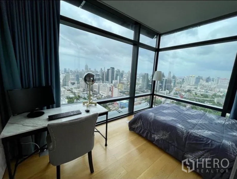 Condominium for sale in Ratchathewi, Bangkok - Second bedroom with study desk by corner glass walls and wide city panorama.
