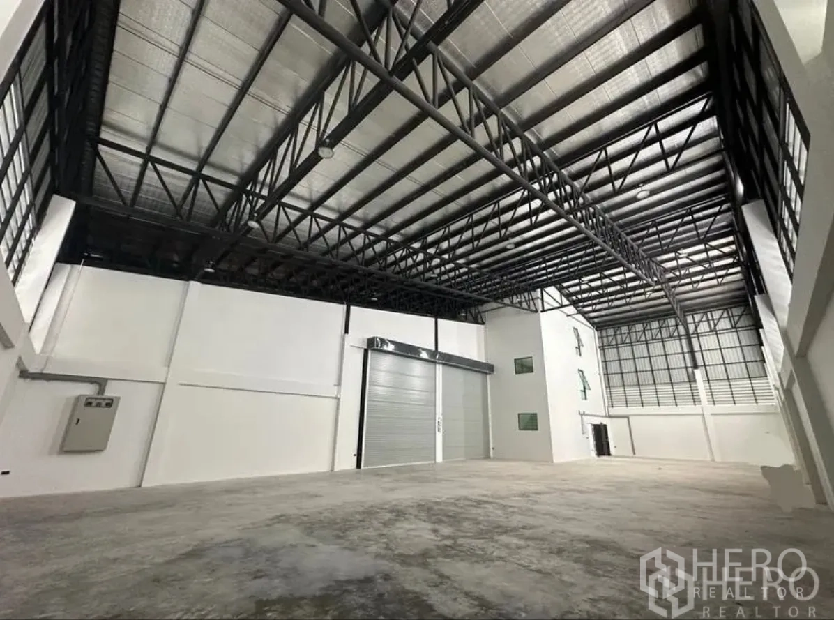 仓库 for sale in Lam Luk Ka, Pathum Thani - 仓库内景：高挑钢桁架屋顶、隔热层与抛光混凝土地面，配大卷闸门。