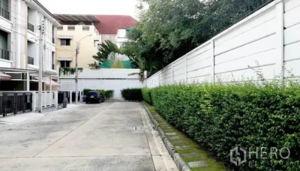 联排别墅 出租在Wang Thonglang, Bangkok - 社区内部安静道路，两侧绿篱与带栅栏的联排住宅及停车位