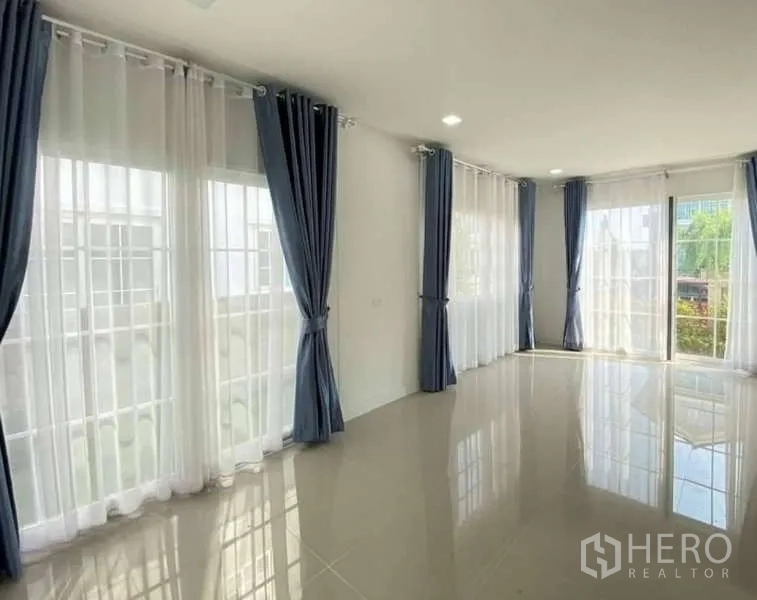 Detached House for sale in Bang Khen, Bangkok - Sunlit corner family room with floor-to-ceiling windows, sheer drapes and garden outlook.