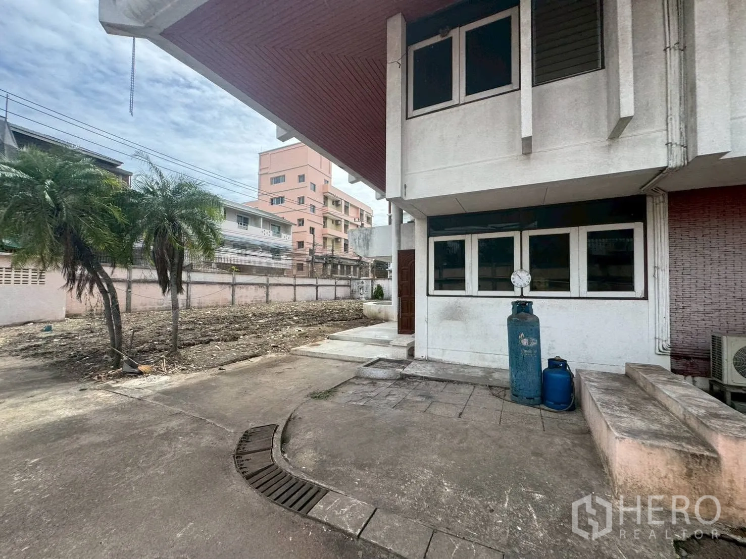 独栋房屋 for rent or sale in Watthana, Bangkok - 侧院清理后的空地，靠墙有两棵棕榈树。