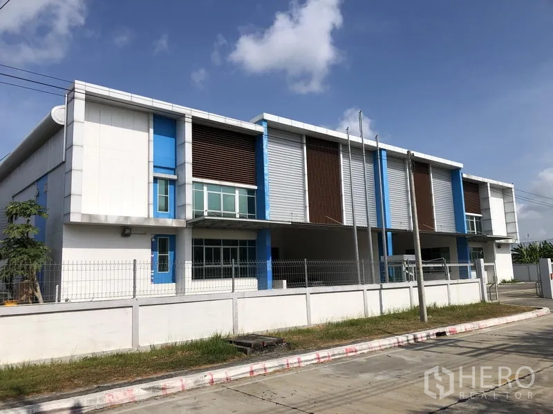 Factory for rent in Bang Sao Thong, Samut Prakan - Modern twin-unit factory exterior with blue accents, fenced perimeter and wide road frontage in Bang Sao Thong.