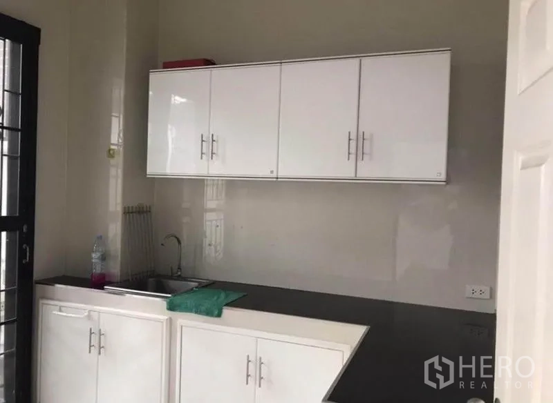 联排别墅 出租在Wang Thonglang, Bangkok - L形厨房，白色橱柜与黑色台面，带水槽和窗边门。