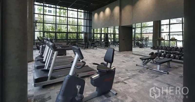 Condominium for rent or sale in Watthana, Bangkok - Resident fitness center with treadmills, stationary bikes, free weights, and large windows.