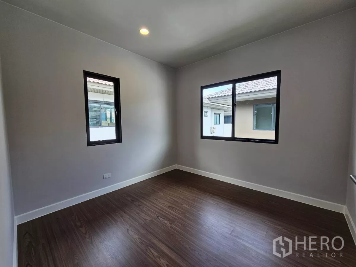 Detached House for sale in Lam Luk Ka, Pathum Thani - Cozy bedroom with two windows and wood flooring.