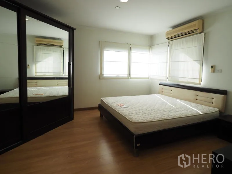 Condominium for rent in Sathon, Bangkok - Sunlit bedroom with corner windows, air conditioner and mirrored wardrobe.