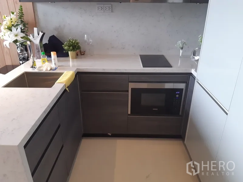 公寓 出租或出售在Watthana, Bangkok - 现代L形厨房，大理石台面，电磁炉、水槽与嵌入式微波炉。