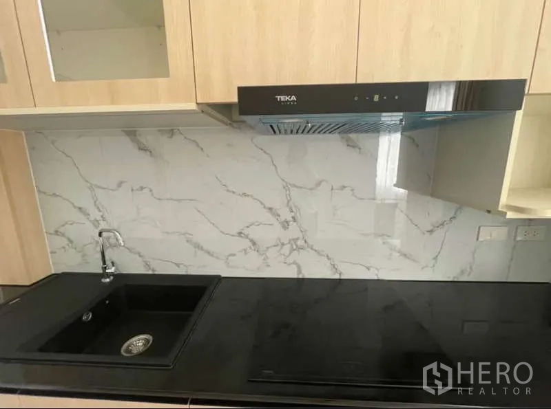 Detached House for rent in Bang Phli, Samut Prakan - Close-up of fitted kitchen with black countertop, sink, hob and hood.