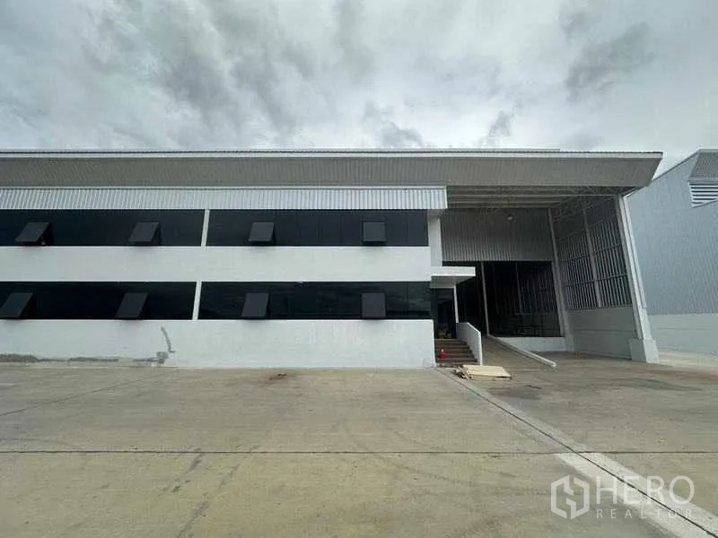 Factory for rent in Wang Noi, Phra Nakhon Si Ayutthaya - Modern factory facade with black ribbon windows, covered loading bay, and wide concrete yard.