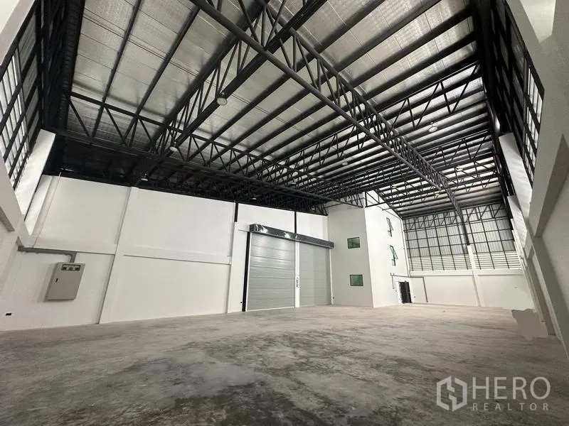 Warehouse for sale in Lam Luk Ka, Pathum Thani - Loading zone view with motorized roller shutter and sturdy steel roof trusses.