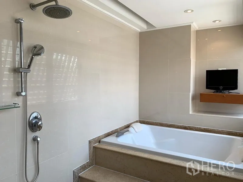 Condominium for sale in Khlong Toei, Bangkok - Bathroom with step-up soaking tub, rain shower and a wall-mounted TV shelf.