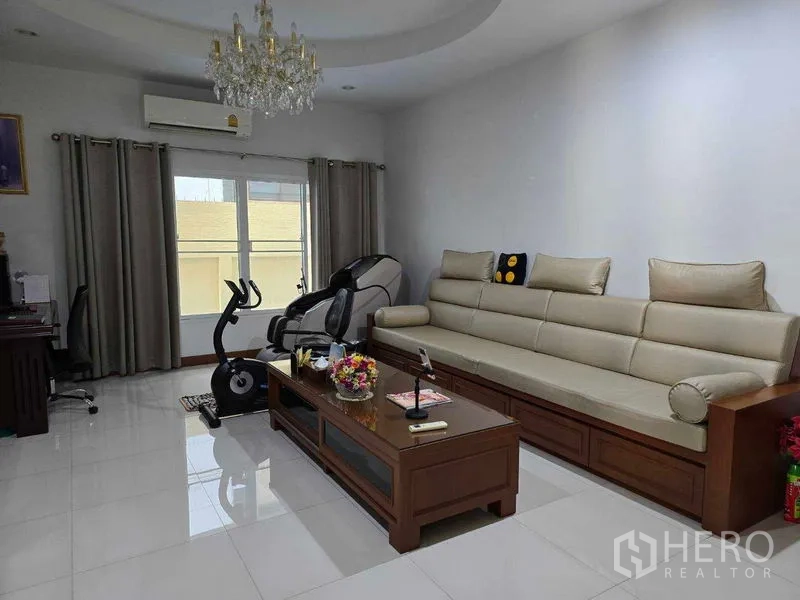 Land for sale - Bright living room with a long sofa, chandelier, and exercise equipment by the window.