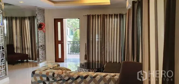 Detached House for sale in Khan Na Yao, Bangkok - Bright living room with patterned sofa, striped curtains, and access to the front patio.