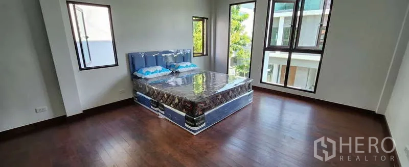 Detached House for rent in Wang Thonglang, Bangkok - Spacious bedroom with multiple windows, wood floors and neighborhood outlook.