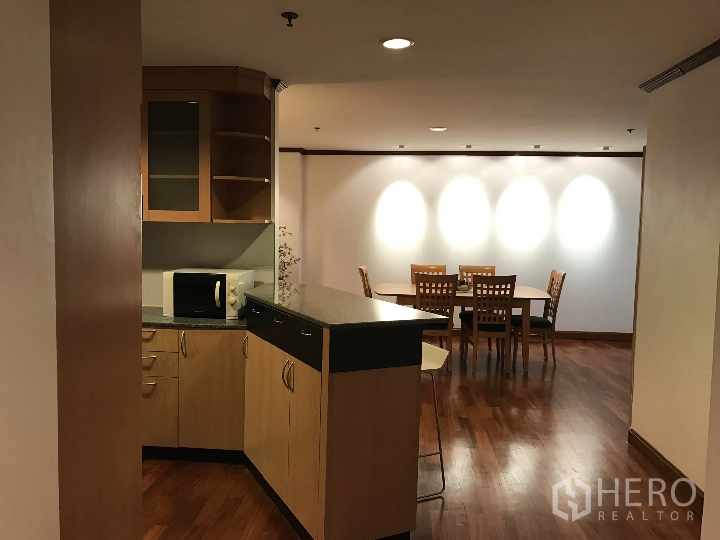 Condominium for rent in Khlong Toei, Bangkok - Kitchen pass-through to dining space with spot lighting and wooden flooring.