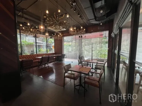 零售空间 出租在Watthana, Bangkok - 餐厅就餐区，皮质长椅、木桌、枝形吊灯，落地窗望向绿植
