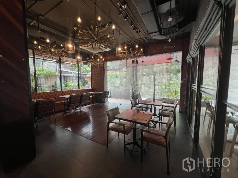 Retail Space for rent in Watthana, Bangkok - Restaurant dining room with leather banquette, wooden tables, chandeliers, and floor-to-ceiling windows overlooking greenery.