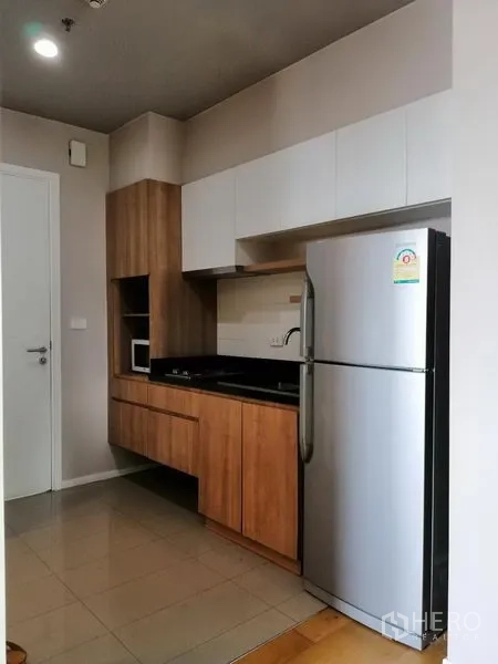 Condominium for rent in Watthana, Bangkok - Compact kitchen with wood cabinets, black countertop and stainless-steel fridge