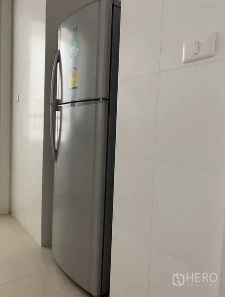 Condominium for rent in Khlong Toei, Bangkok - Stainless steel refrigerator against a white tiled kitchen wall.