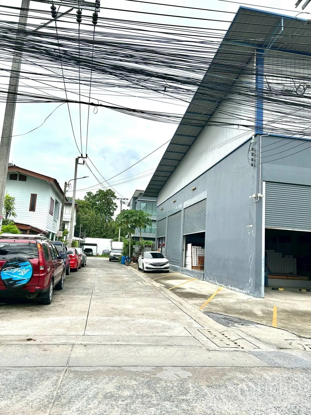 Warehouse for rent in Suan Luang, Bangkok - Side street view of the warehouse with multiple shutters and roadside parking.