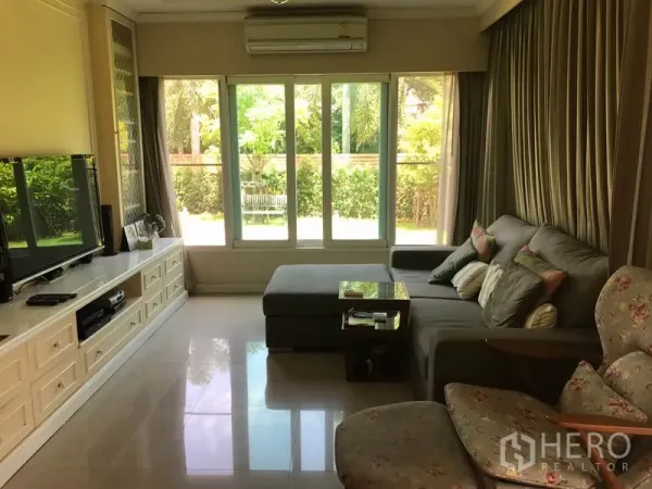 独立式住宅 出售在Pak Kret, Nonthaburi - 宽敞起居室，L形沙发、落地玻璃，眺望花园。