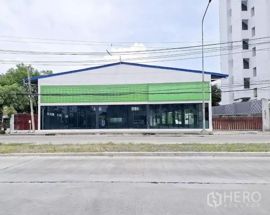 Warehouse for rent in Bang Kapi, Bangkok - Street-facing warehouse with glass showroom frontage and green facade panels on a main road in Bang Kapi, Bangkok.