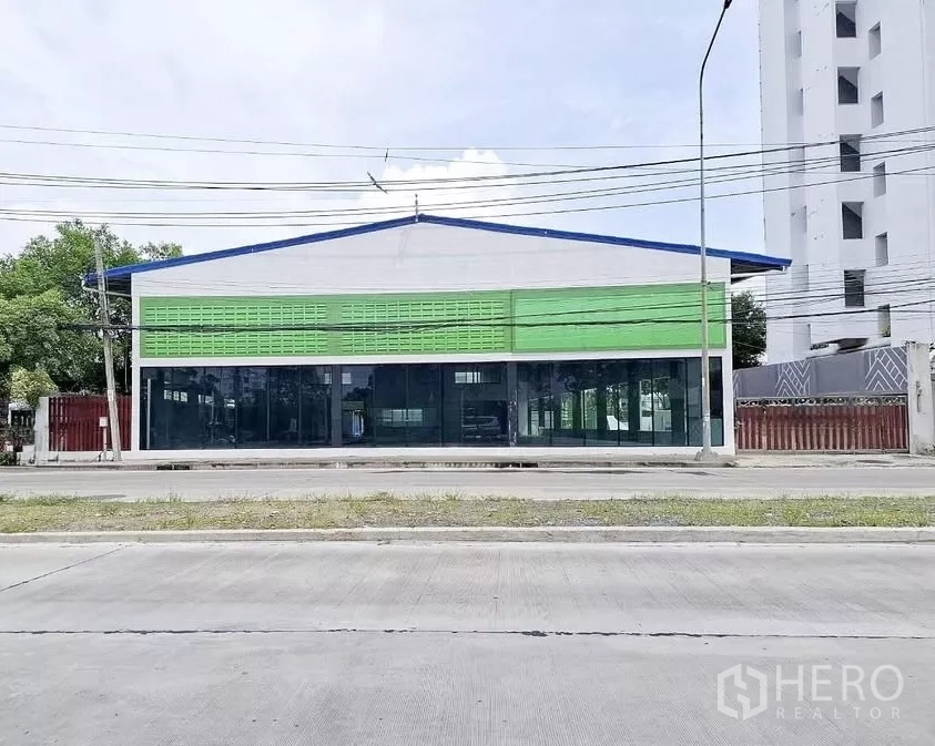 Warehouse for rent in Bang Kapi, Bangkok - Street-facing warehouse with glass showroom frontage and green facade panels on a main road in Bang Kapi, Bangkok.