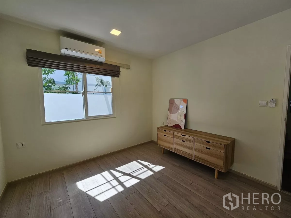 Detached House for rent in Bang Phli, Samut Prakan - Sunlit ground-floor room with air conditioning and a low wooden sideboard.