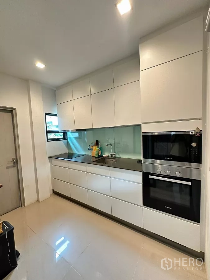 Detached House for rent in Saphan Sung, Bangkok - Modern closed kitchen with white cabinetry, glass backsplash and built-in oven and cooktop.