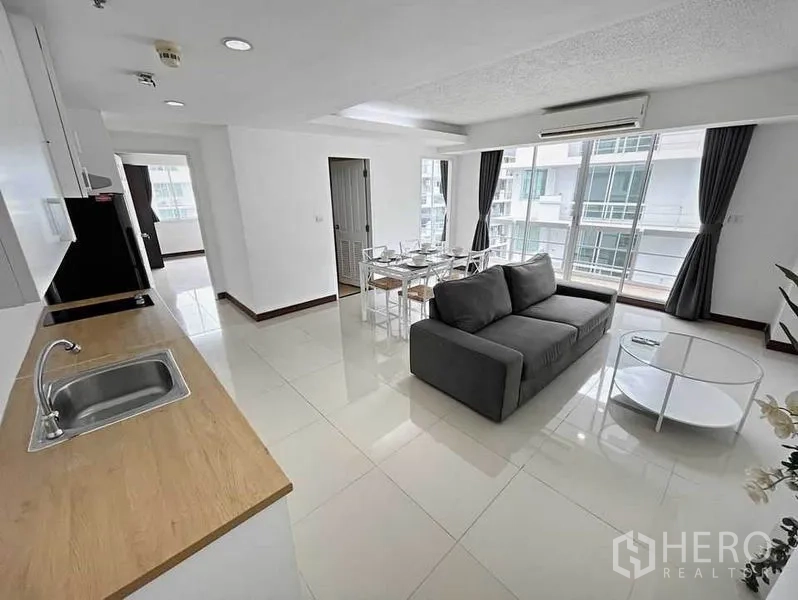 Condominium for rent in Khlong Toei, Bangkok - Open kitchenette with wood countertop, white cabinets and fridge facing the living–dining zone.
