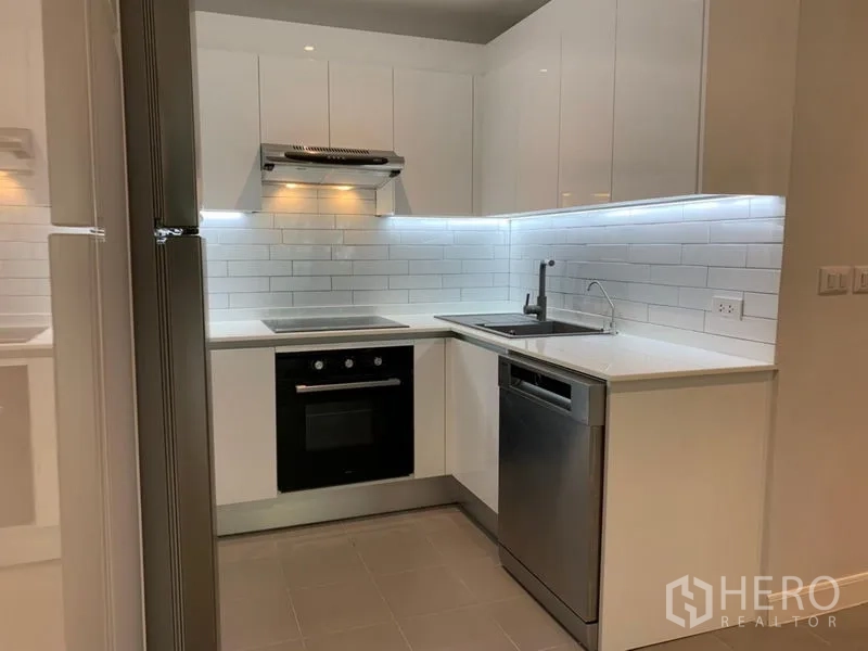 Condominium for sale in Watthana, Bangkok - L-shaped kitchen with electric cooktop, oven, sink and dishwasher.