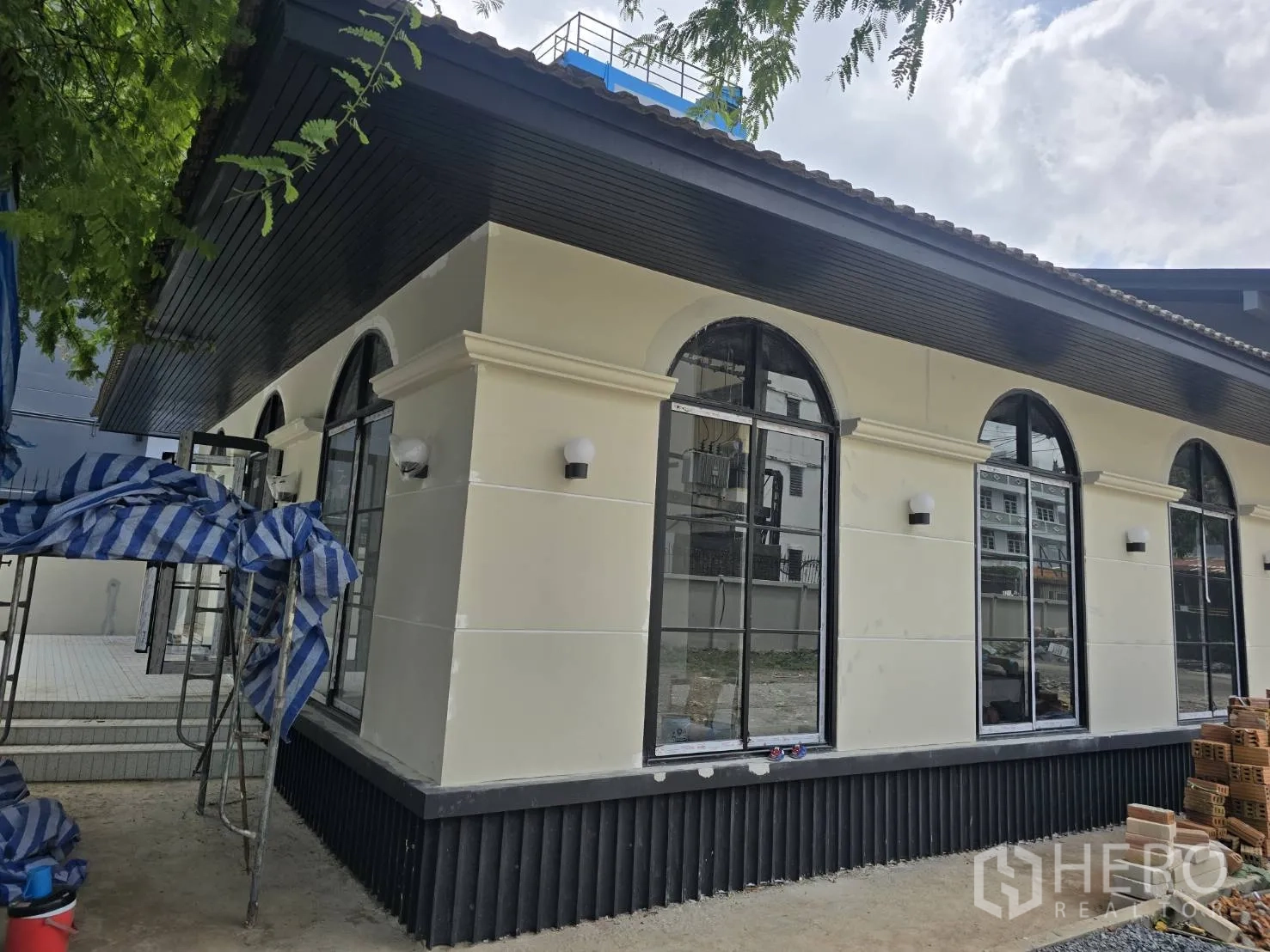 家庭办公室 for rent in Phra Khanong, Bangkok - 建筑转角外立面，奶油色墙体与多扇拱形窗，屋檐突出。