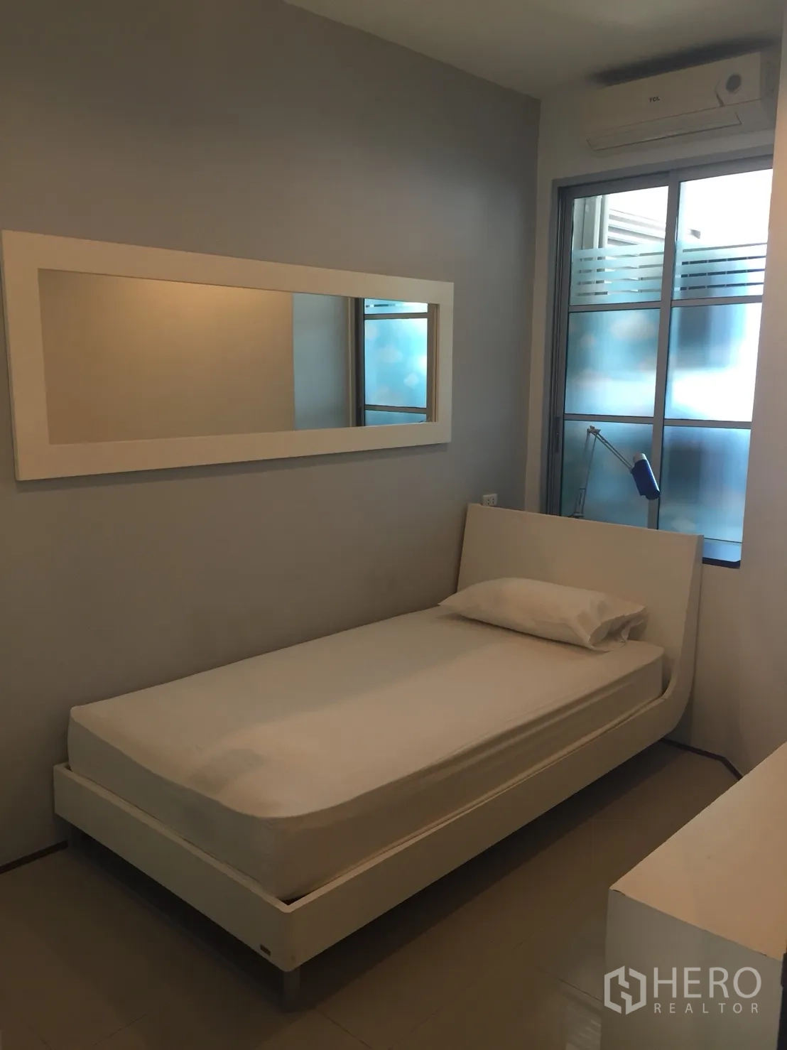 Condominium for rent in Khlong Toei, Bangkok - Compact second bedroom with single bed, long wall mirror, air conditioner, and frosted-glass window.