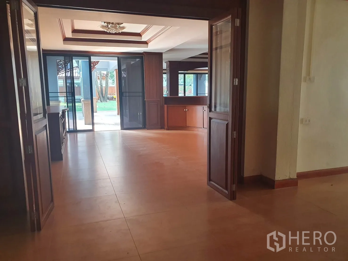 独栋房屋 for rent in Sathon, Bangkok - 宽阔客厅，瓷砖地面，木质柜体，推拉玻璃门通向花园。