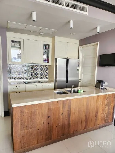 Condominium for sale in Khlong Toei, Bangkok - Kitchen island with wood cladding, white cabinetry and stainless refrigerator.