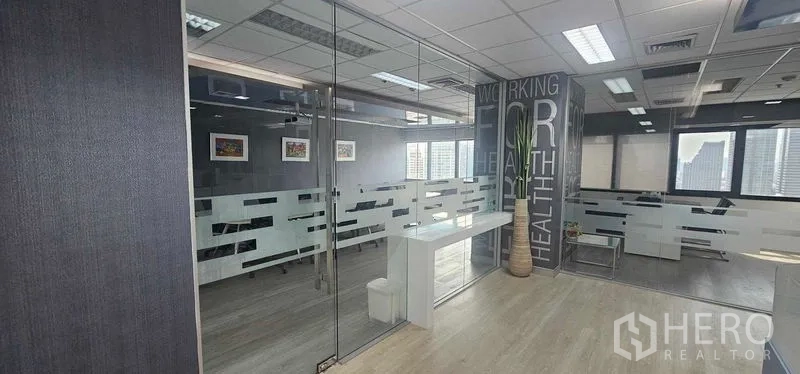 Office Space for rent in Bang Rak, Bangkok - Open office zone with glass partitions, wall graphic, potted plant and large windows in a modern Silom workplace.