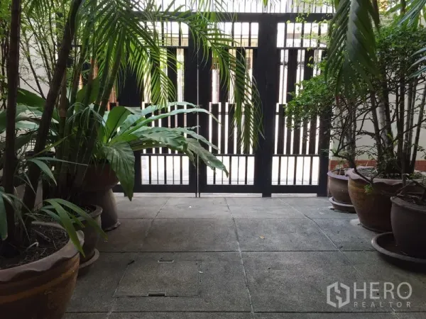 ทาวน์เฮาส์ ให้เช่าในWatthana, Bangkok - ลานหน้าบ้านร่มรื่น มีต้นไม้กระถางและประตูรั้วเหล็กสีดำ