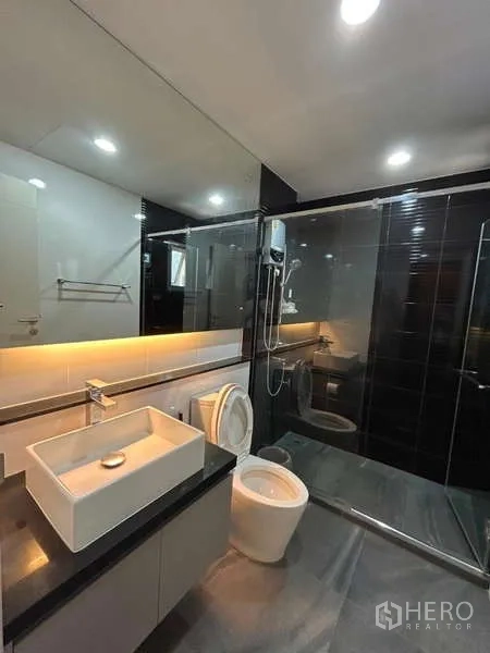 Detached House for rent in Bang Kapi, Bangkok - Sleek bathroom with black tiled shower, wide mirror, and counter with vessel sink.