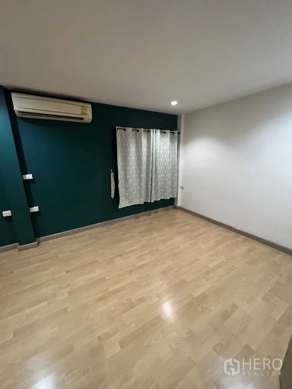 联排别墅 出租在Watthana, Bangkok - 卧室一角，孔雀绿墙、空调与浅色木地板。