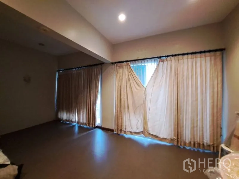 Shophouse for rent in Watthana, Bangkok - Large dim room with wide windows covered by curtains.