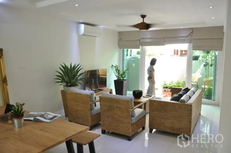 联排别墅 出租或出售在Watthana, Bangkok - 客厅配电视与藤编家具，通过推拉玻璃门通向花园露台。