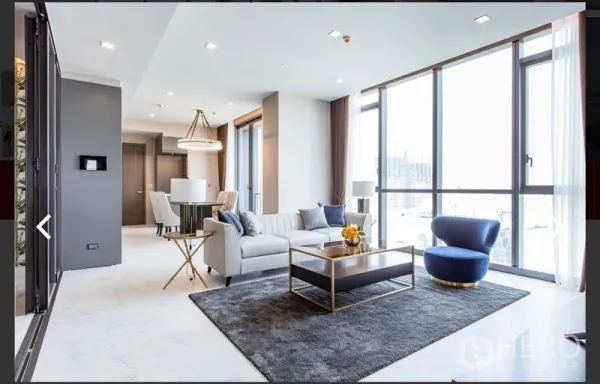 Condominium for rent or sale in Watthana, Bangkok - Open-plan living and dining room with large windows, gray sofa, blue lounge chair, and modern chandelier.
