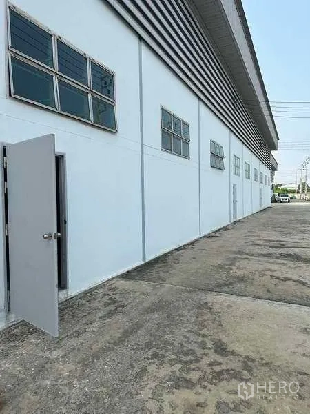 Warehouse for rent in Bang Phli, Samut Prakan - Side exterior walkway of the building with windows and a service door.