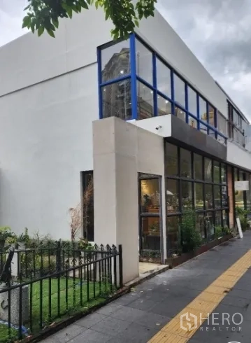 Retail Space for rent in Khlong Toei, Bangkok - Two-storey retail corner with blue-framed windows and landscaped verge along the footpath in the Ekkamai area.