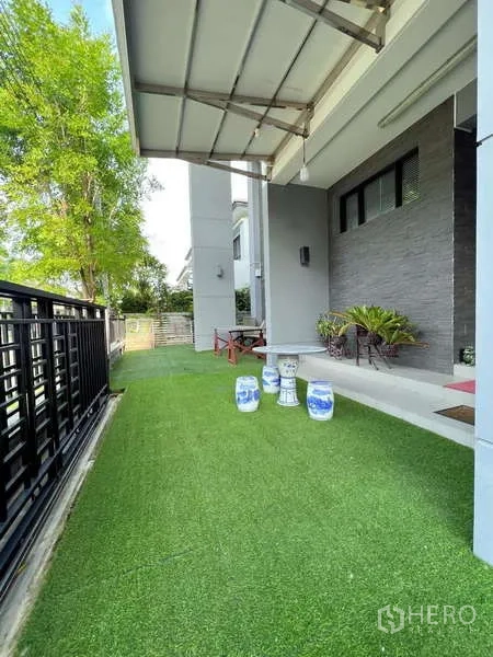 独立式住宅 出售在Prawet, Bangkok - 侧院人工草坪，带顶棚的露台与盆栽点缀篱笆。